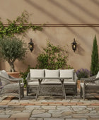 Outdoor patio set with cushions on a stone patio, surrounded by plants and wall lights.