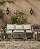 Outdoor patio set with wicker furniture on a stone patio surrounded by plants.
