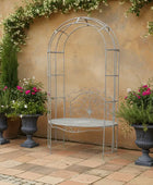 Metal garden arch with bench against a beige wall with potted plants.