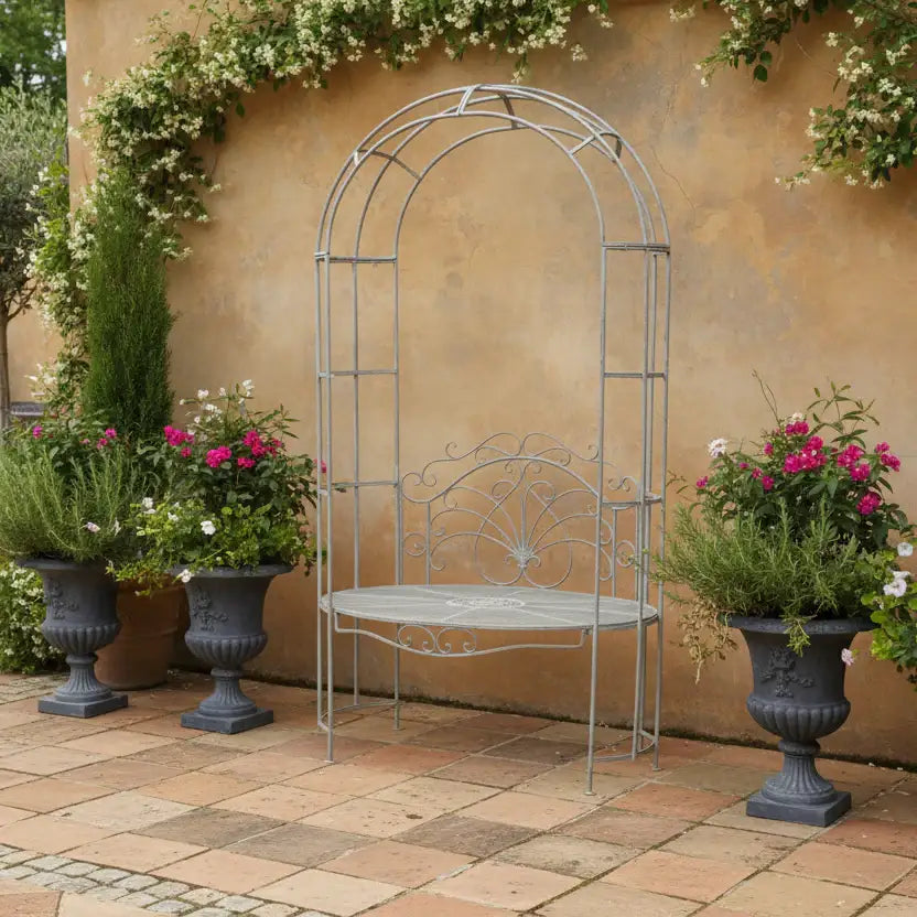 Metal garden arch with bench against a beige wall with potted plants.