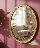 Decorative round mirror with floral design on a pink wall, reflecting a living room.