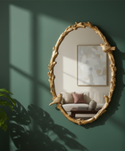 Decorative gold-framed mirror on a green wall with a couch and plant in the background