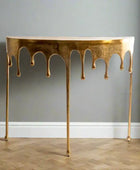 Gold console table with a unique design on a wooden floor and gray wall background