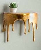 Decorative wall shelf with gold metallic finish and dripping effect on a white background