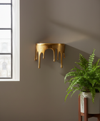 Gold wall-mounted shelf with a plant on a gray wall