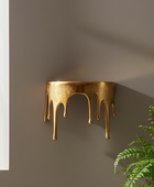 Gold wall-mounted lamp with a modern design on a gray wall next to a window and plant.