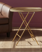 Gold side table with decorative tray next to a brown leather sofa against a purple wall.