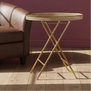 Gold side table with decorative tray next to a brown leather sofa against a purple wall.