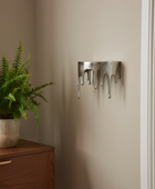 Metal wall art piece on a beige wall next to a wooden cabinet with a plant.
