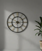 Large wall clock with gold accents on a gray wall next to a potted plant.