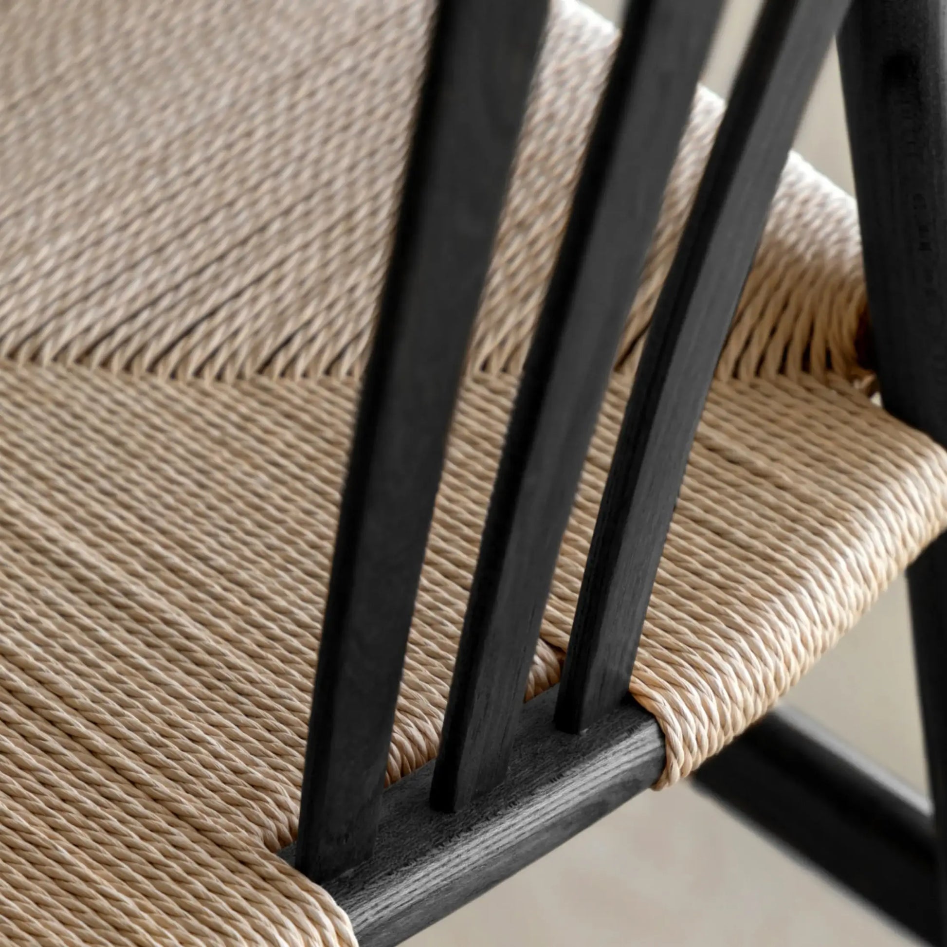 Close-up of a chair with woven seat and black wooden frame.