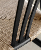 Close-up of a chair with woven seat and black wooden frame.
