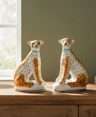 Two ceramic cheetah figurines on a wooden surface with a window and plant in the background.