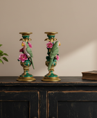 Decorative candle holders with birds and flowers on a wooden surface with a plant and book in the background.