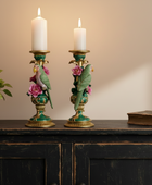 Decorative candle holders with parrot and flower designs on a wooden surface.