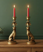 Two gold cheetah-shaped candle holders with red candles on a wooden surface against a green wall.