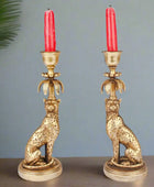 Pair of gold cat-shaped candle holders with red candles on a gray background