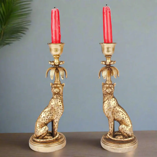 Pair of gold cat-shaped candle holders with red candles on a gray background