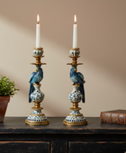 Decorative candlesticks with birds on a wooden surface against a beige wall.