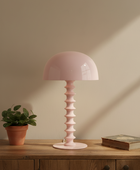 Pink table lamp on a wooden surface with a plant and book in the background
