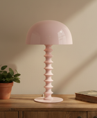 Pink table lamp on a wooden surface with a plant and book in the background