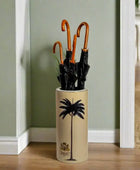 Beige umbrella stand with black palm tree design holding four black umbrellas on a white background