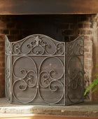 Decorative metal fireplace screen in front of a brick fireplace with a plant to the right.