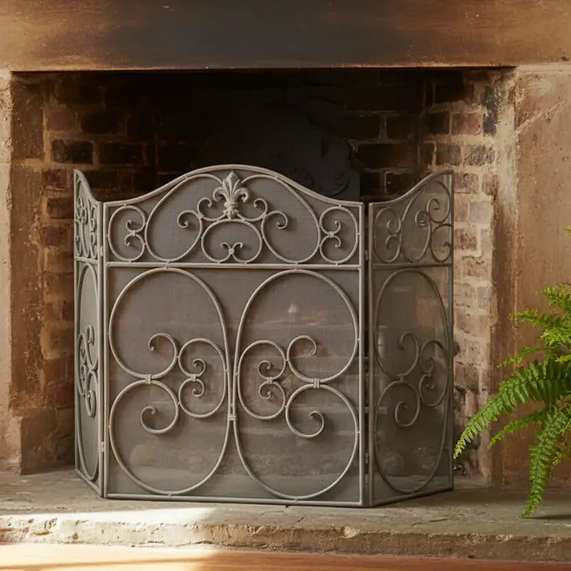 Decorative metal fireplace screen in front of a brick fireplace with a plant to the right.