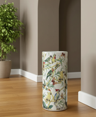 Decorative umbrella stand with bird pattern on a wooden floor next to a plant.