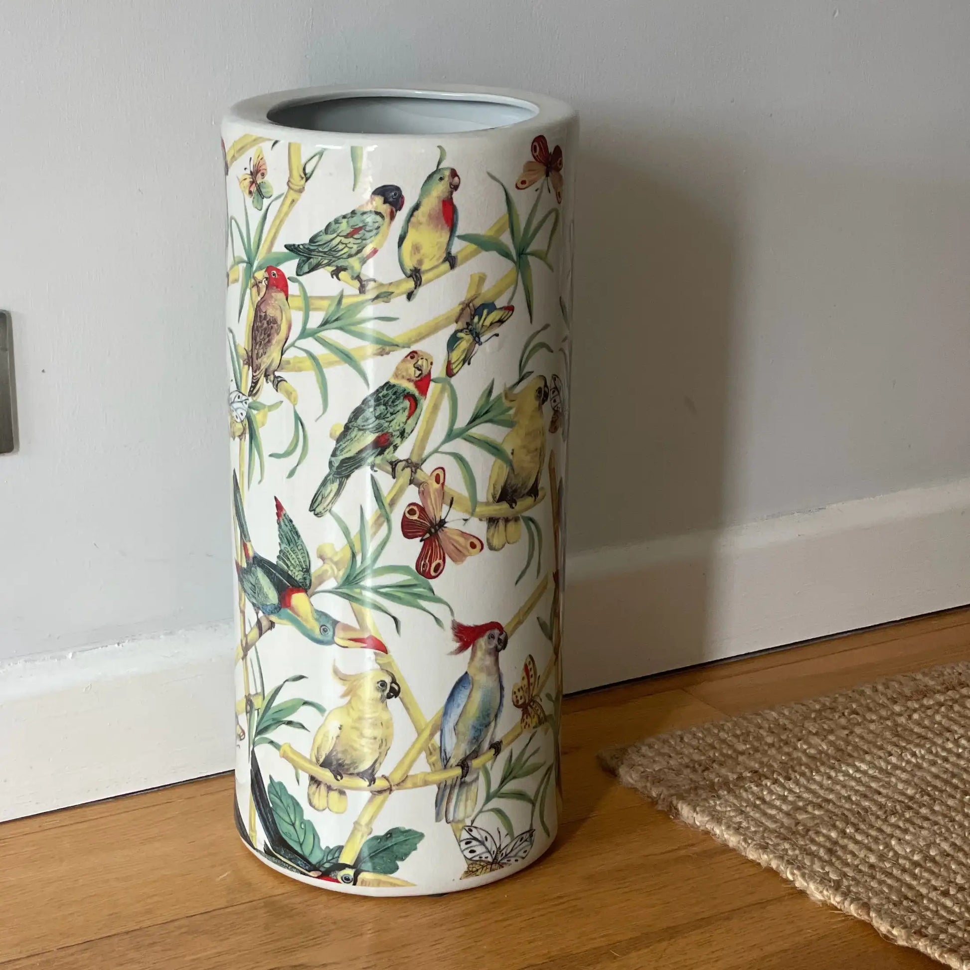 Umbrella stand with bird design on a wooden floor against a white wall.