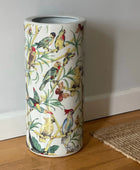 Umbrella stand with bird design on a wooden floor against a white wall.