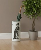 Umbrella stand with penguin design holding an umbrella next to a potted plant on a wooden floor.