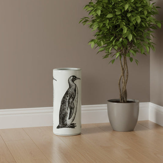Cylindrical vase with penguin design next to a potted plant on a wooden floor.