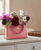 Pink handbag filled with flowers on a wooden surface with a window in the background