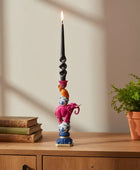 Decorative candle holder with colorful design on a wooden surface with books and a plant.
