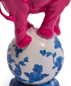Pink elephant standing on a white vase with blue floral patterns on a white background