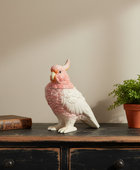 Decorative parrot sculpture on a wooden surface with a plant and book in the background.