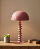 Pink table lamp on a wooden surface with a plant and book in the background