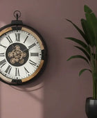 Decorative wall clock with Roman numerals on a pink wall next to a potted plant.