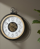 Decorative wall clock with gear detail on a beige wall, next to a plant.