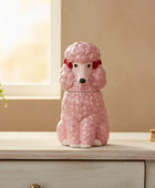 Pink poodle-shaped container on a wooden surface with a plant and book in the background.