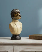 Decorative bust of a dog in a pilot helmet on a wooden surface with a plant and book in the background.