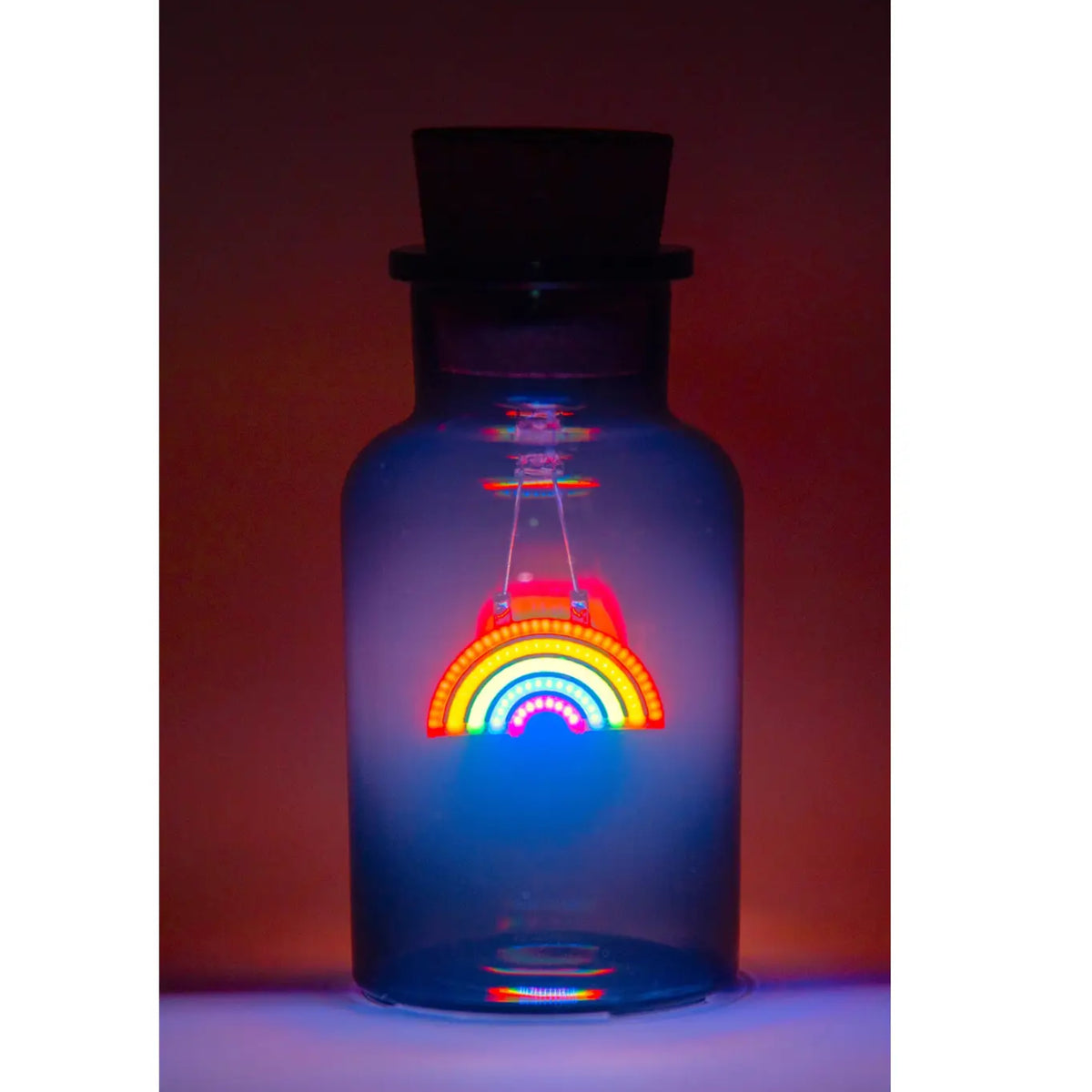 A small glass bottle with a dark stopper, glowing with blue light and featuring a colorful rainbow design in the center.