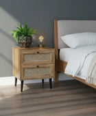 Wooden nightstand with rattan drawers, lamp, and plant against a gray wall.