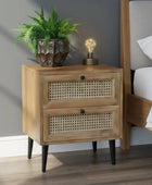 Wooden nightstand with two drawers, a potted plant, and a lamp in a bedroom setting.