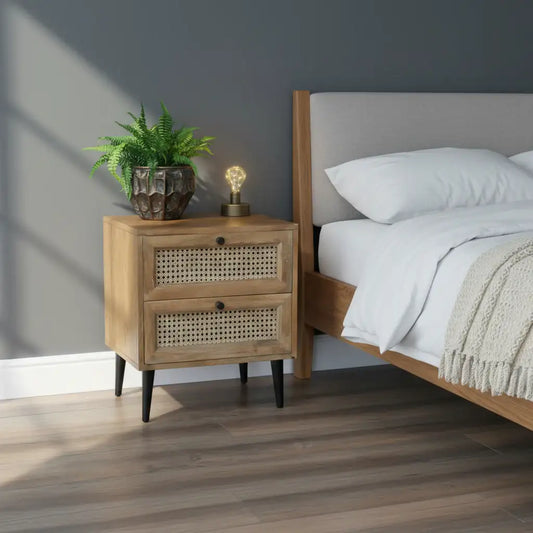Wooden nightstand with rattan drawers, lamp, and plant against a gray wall.