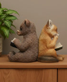 Two animal figurines, one resembling a bear and the other a fox, sitting on a wooden surface with books.