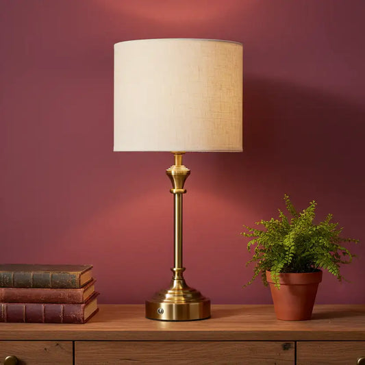 Brass table lamp with white shade on a wooden surface against a red wall