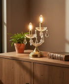 Decorative table lamp with crystal accents on a wooden surface next to a plant and book.