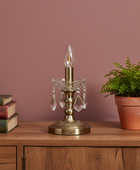 Decorative table lamp with crystal accents on a wooden surface next to books and a plant against a pink wall.
